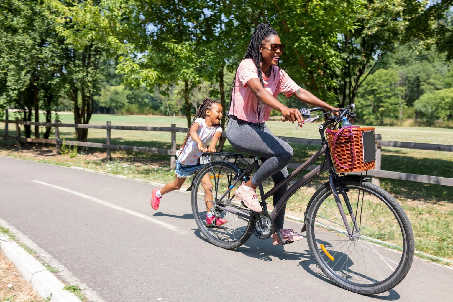 Een vrouw fietst lachend door een groene omgeving, met een kind dat naast haar rent.