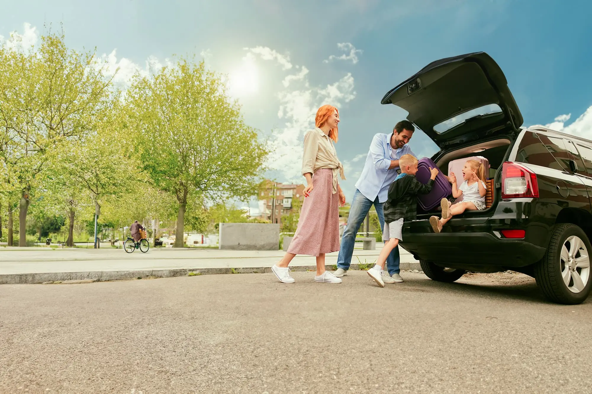 Een gezin bij een geparkeerde auto, met een fietser op de achtergrond